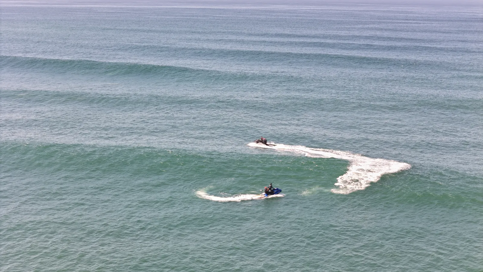 Linee di swell pulite viste dall'alto, due jetski e le loro scie