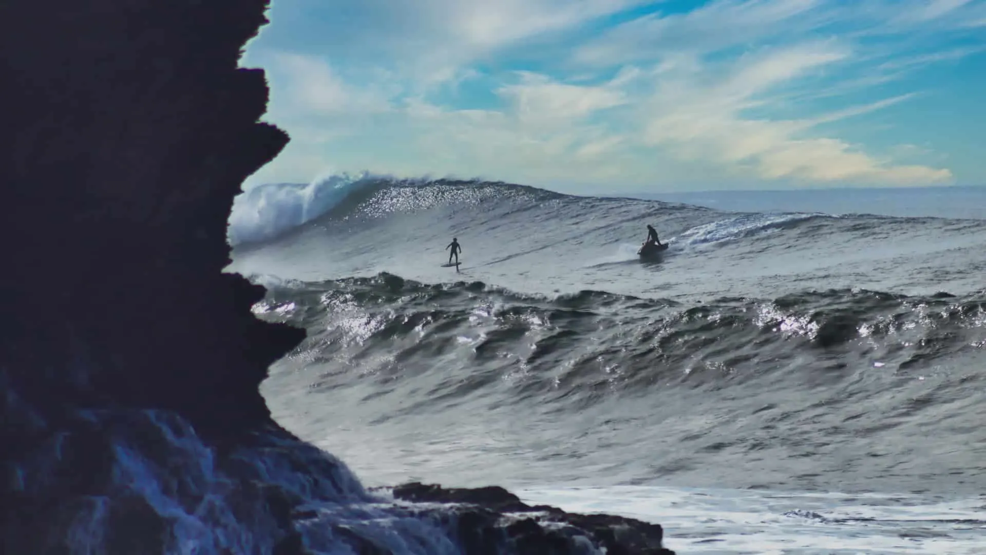 A serious Atlantic day: foiler and ski behind a heaving wave, cliffs in the foreground