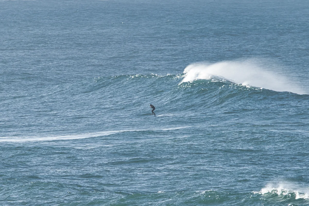 Foiler dropping into a wave while offshore wind blows the spray back